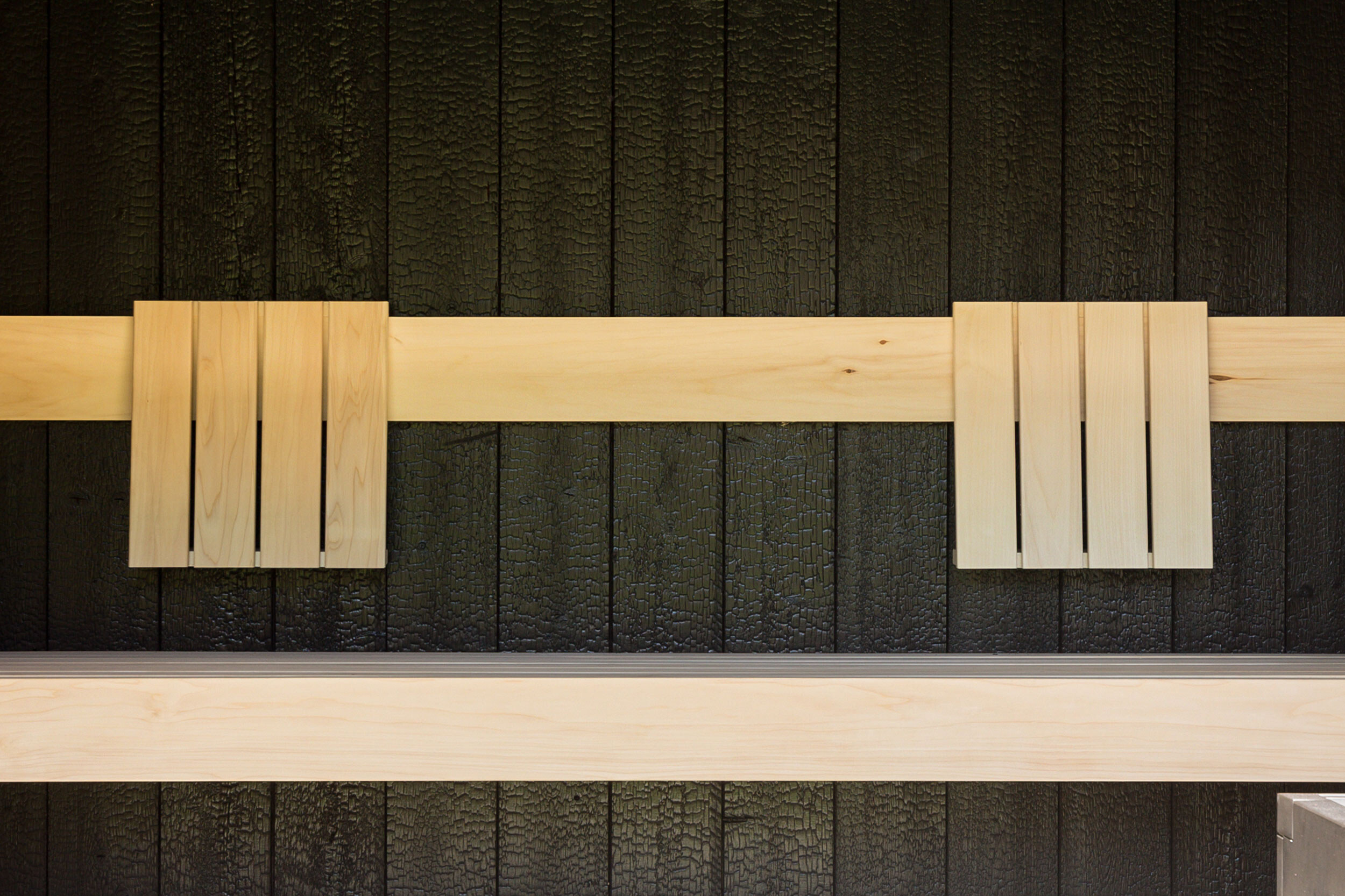 Massive Zirbenholz-Sauna mit vertikalem Fugenbild, schwarzer Lärchenholzverkleidung und Übereckverglasung.